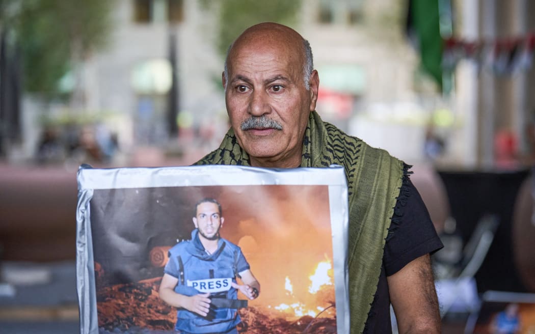 A man holds a portrait of the late Palestinian journalist Anas Al-Sharif as he gathers for a vigil to commemorate all journalists killed in Gaza, at the Ministry of Foreign Affairs in The Hague, on August 11, 2025. (Photo by Phil Nijhuis / ANP / AFP) / Netherlands OUT / NETHERLANDS OUT / NETHERLANDS OUT
