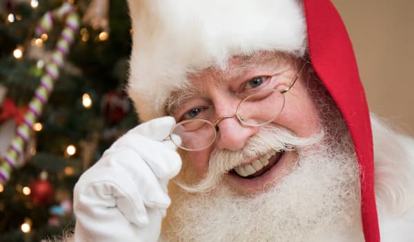 A close up portrait of Santa with a Christmas tree in the background.