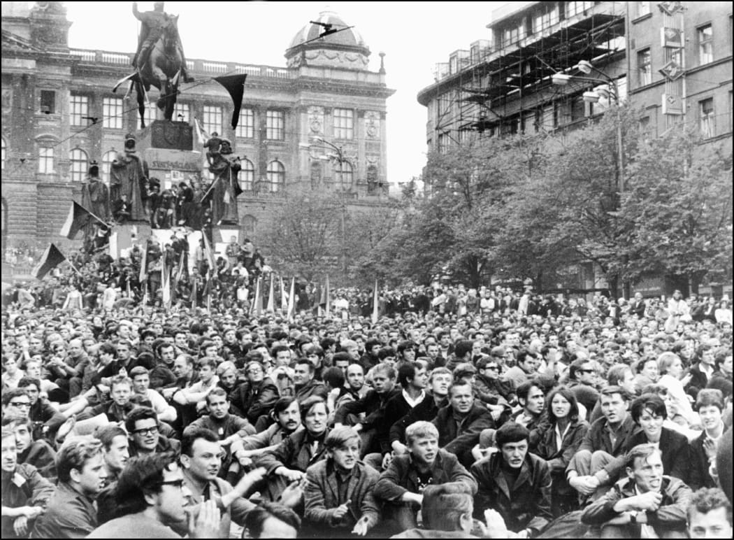 Prague residents hold Czechoslovakian flags in Wenceslas Square during confrontations between demonstrators and Warsaw Pact troops and tanks.