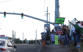 Demonstrators in Dededo, Guam, holding signs with various messages during the 2025 No King's rally.