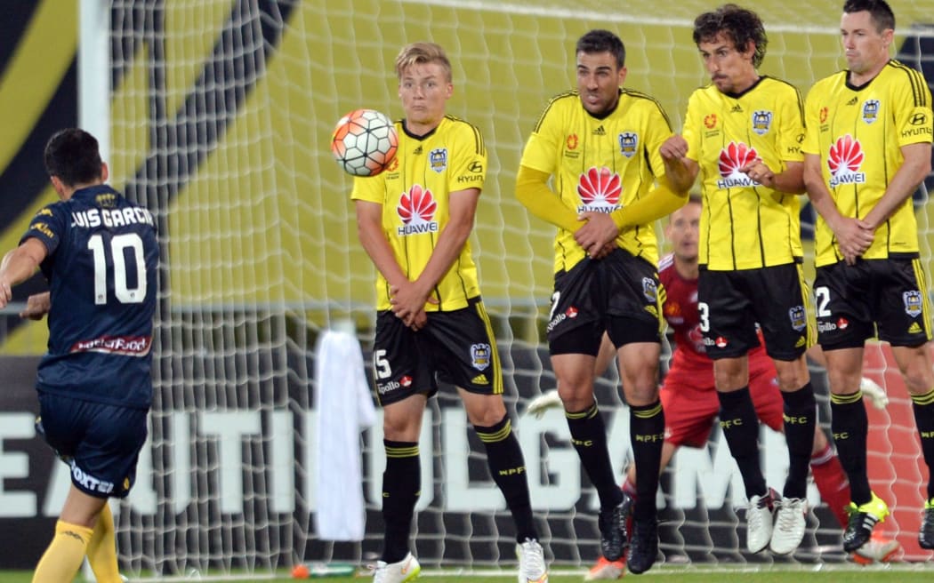 Luis Garcia of the Mariners shooting a free-kick and James McGarry, Manny Muscat, Albert Riera Vidal and Blake Powell of the Phoenix (L-R) reacting.