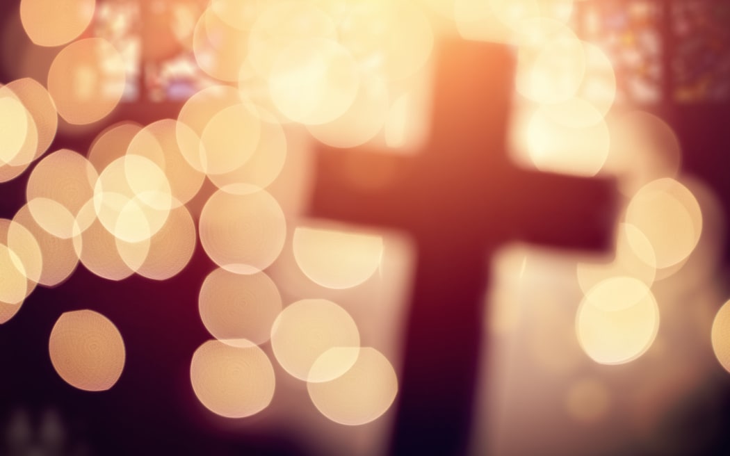 Abstract defocussed cross silhouette in church interior against stained glass window.