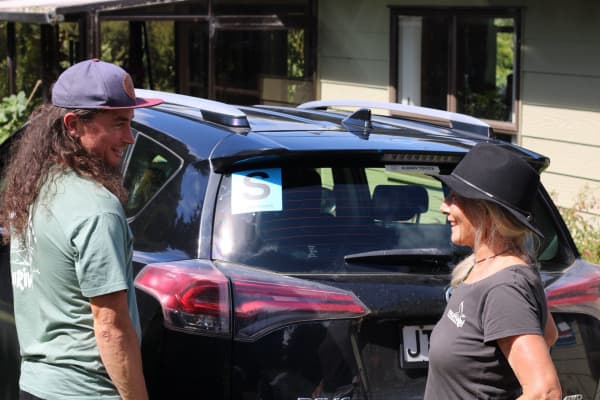 Boyd Steel standing with a friend outdoors near her car, which displays an 's' sticker in blue.
