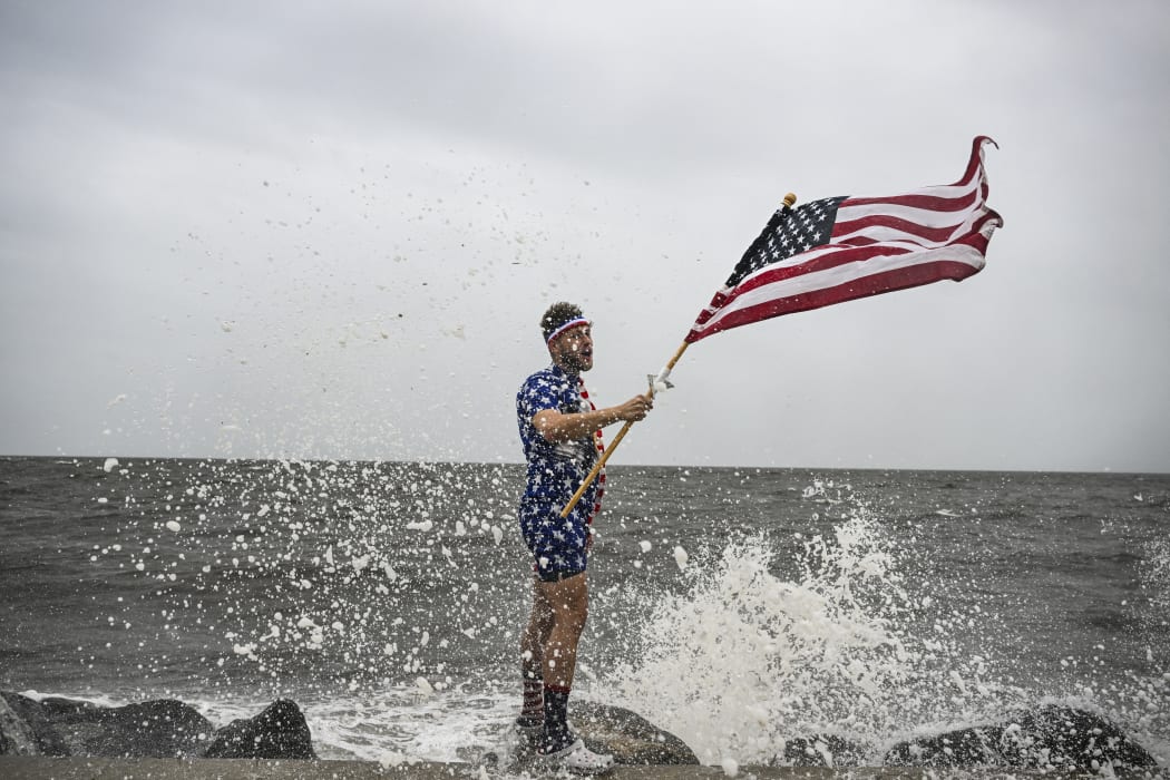 Youtuber Mark Peyton holds a US flag as he poses for his brother Matt Peyton on the shoreline ahead of the arrival of Hurricane Helene in Alligator Point, Florida, on September 26, 2024. Parts of Florida face "unsurvivable" conditions when Hurricane Helene hits later Thursday, the US weather service said, warning that howling wind will drive destructive waves and storm surge as high as 20 feet (six meters) onto the low-lying coast. Residents heeded mass evacuation orders and fled ahead of the incoming hurricane -- projected to be one of the largest Gulf of Mexico storms in decades. (Photo by CHANDAN KHANNA / AFP)