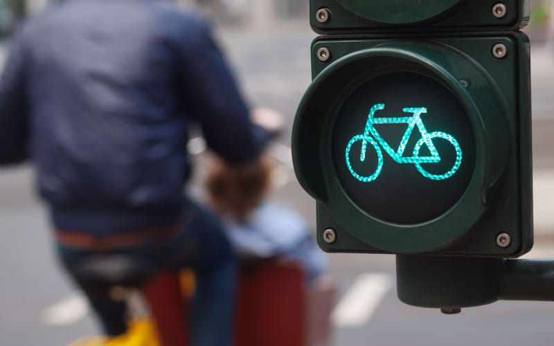 A cyclist passes a green cycling traffic light in a city.