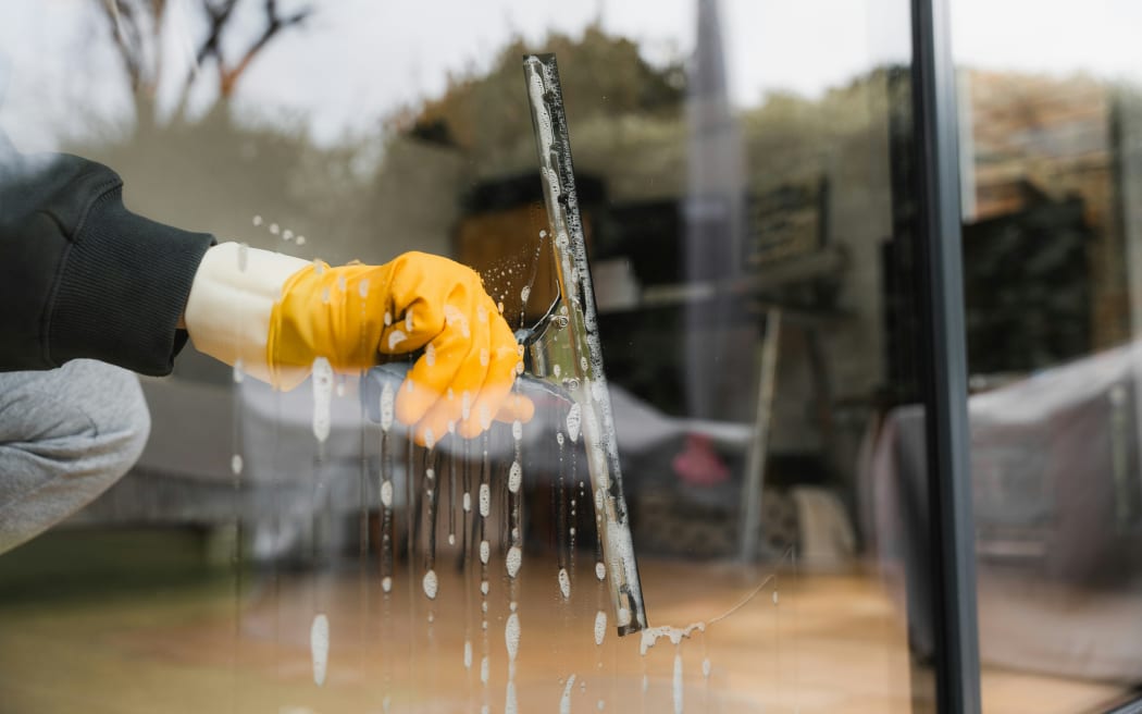 A hand in a yellow plastic glove cleans a window with a squeegee.