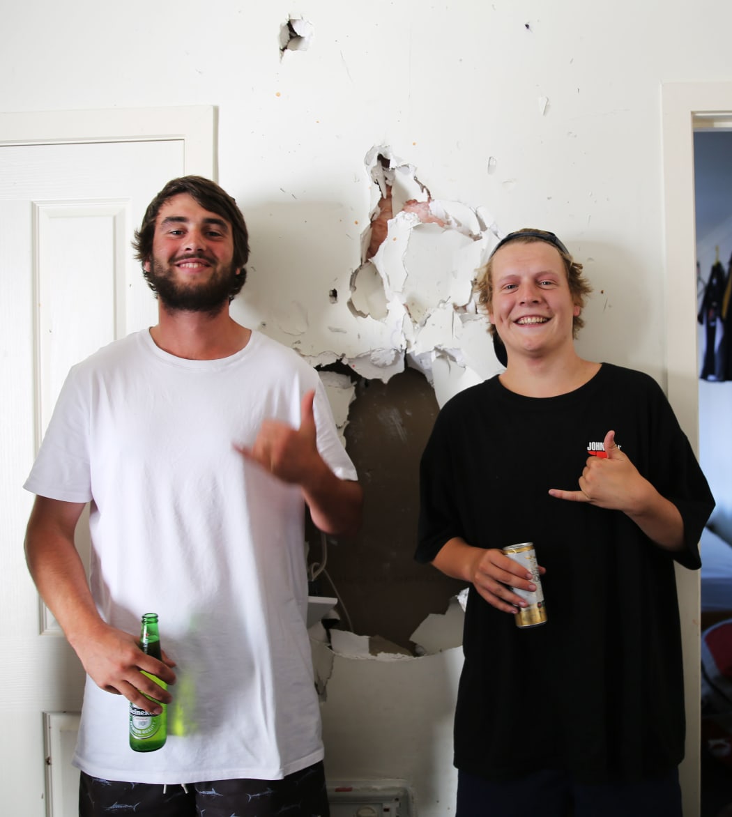 Max Lynch and Speedy pose next to a hole in their living room wall.