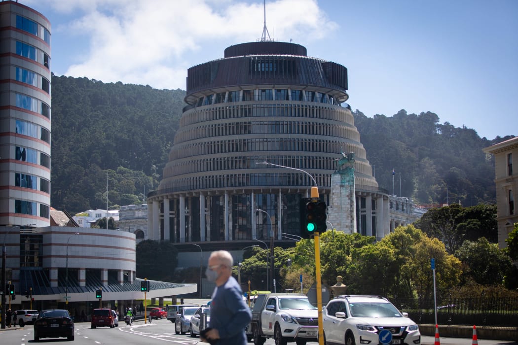 A man wearing a mask crosses the street in front of Parliament