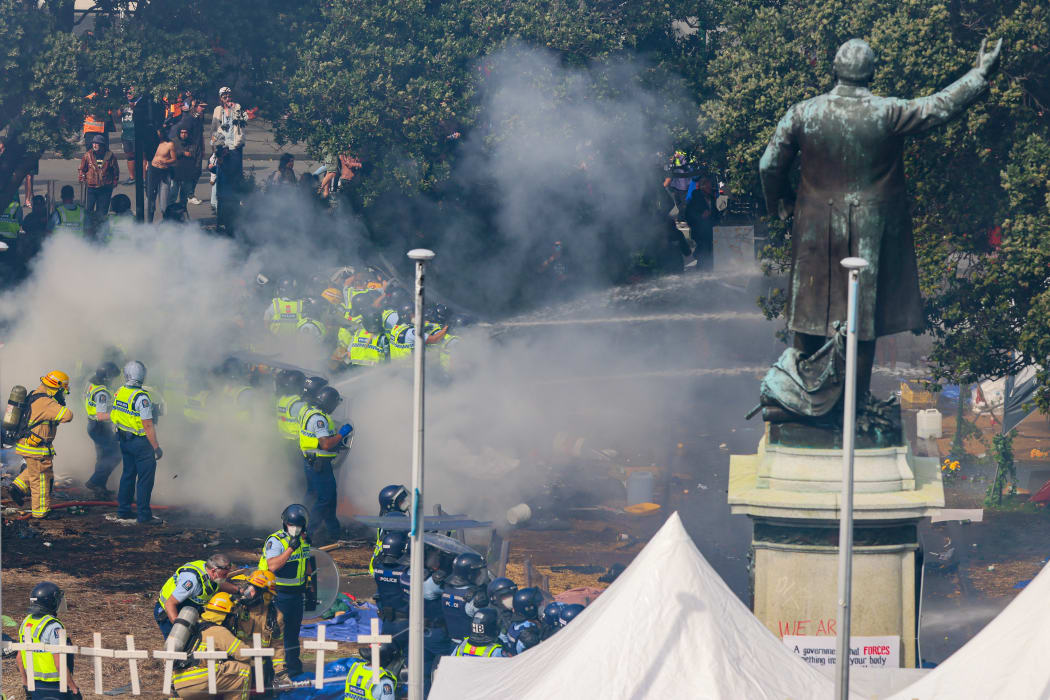Police stand in the hot embers of the first fire to aim hoses at the second.