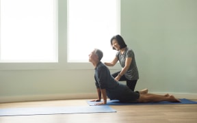 Side view of mature couple doing yoga push up, correcting posture (Photo by David Jakle / Connect Images via AFP)