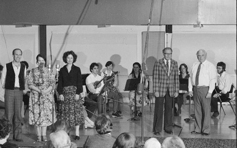 Douglas Lilburn (fourth from righ, in checked jacket), Ashley Heenan (2nd from right on stage), and members of the Schola Musica at a special broadcast concert honouring Douglas Lilburn on his 65th birthday, in Symphony House, Willis Street, Wellington. November 1980.