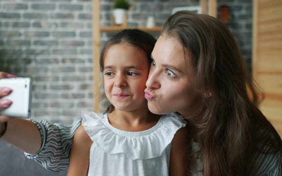 A young girl and her mother make faces for a selfie taken by the mother.