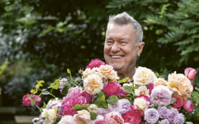 Jimmy Barnes smiles widely and holds a large bunch of beautiful roses.