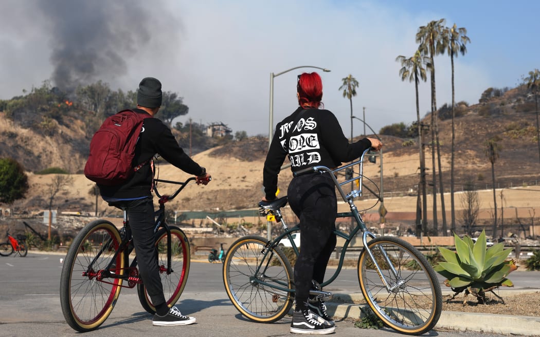 PACIFIC PALISADES, CALIFORNIA - JANUARY 09: People watch as a home burns during the Palisades Fire on January 09, 2025 in Pacific Palisades, California. Multiple wildfires fueled by intense Santa Ana Winds are burning across Los Angeles County. At least five people have been killed, and over 25,000 acres have burned. Over 2,000 structures have also burned and almost 180,000 people are under orders to evacuate. (Photo by Mario Tama/Getty Images)