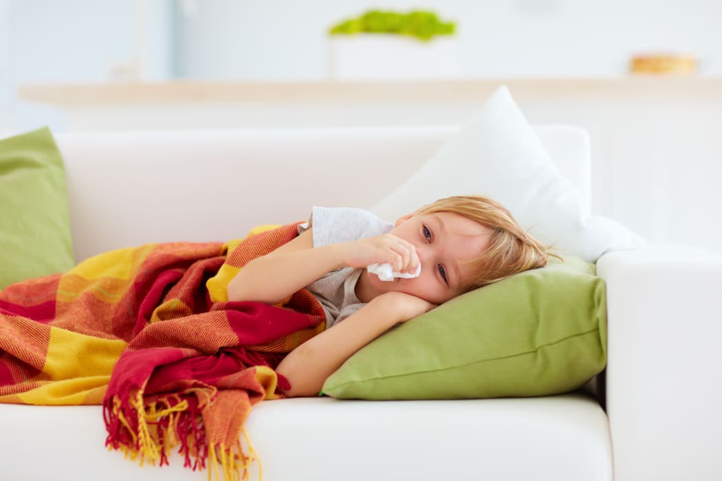 sick kid with runny nose and fever heat lying on couch at home