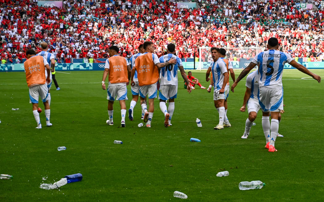 Argentina's forward #17 Giuliano Simeone (2ndR) looks on as water bottles thrown by Morroco's fans litter the pitch after Argentina scored their second goal, which was cancelled after a two-hour interruption, in the men's group B football match between Argentina and Morocco during the Paris 2024 Olympic Games at the Geoffroy-Guichard Stadium in Saint-Etienne on July 24, 2024. (Photo by Arnaud FINISTRE / AFP)