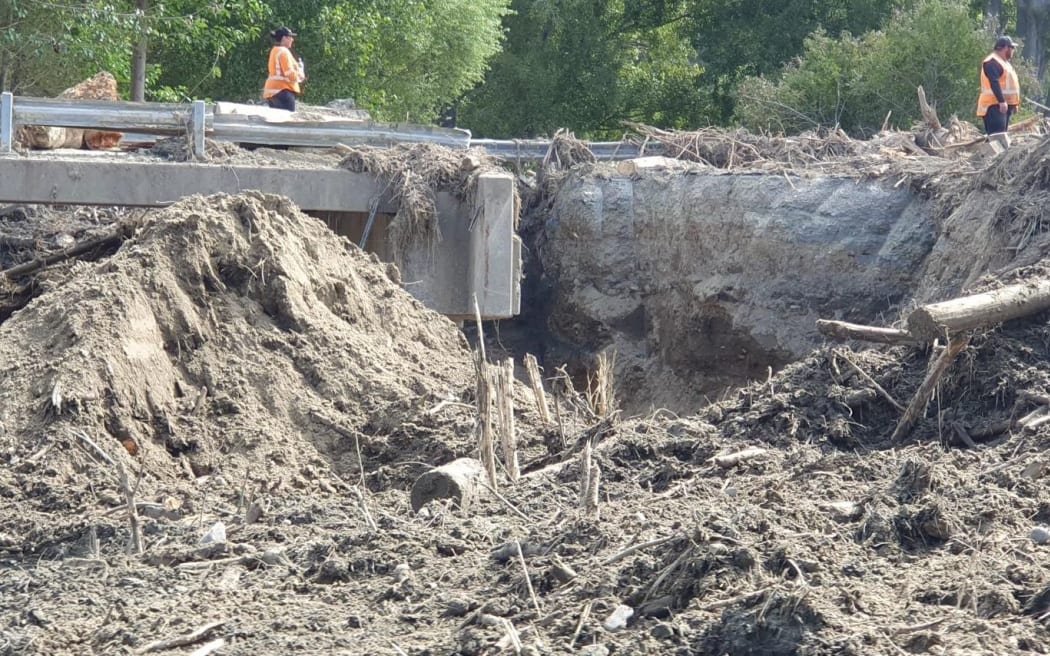 Roadworkers stand either side of a 2m wide, 3m deep gash across the width of SH5 adjacent to Marshall's Bridge near Glengarry. A crossing to the side allows contractors' vehicles across.