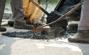 Two construction workers working together to patch a bump in the road with fresh asphalt.