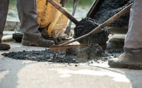 Two construction workers working together to patch a bump in the road with fresh asphalt.