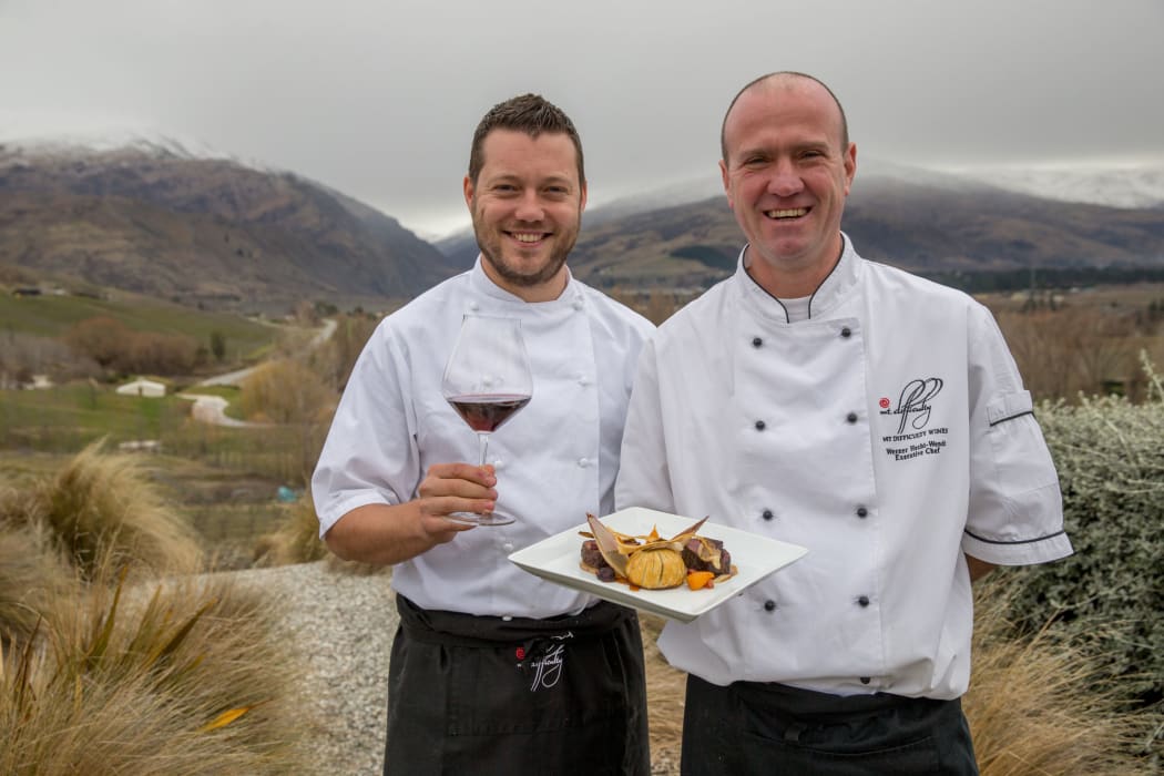 Mark Southon and Werner Hecht-Wendt with dish and wine in front of Mount Difficulty