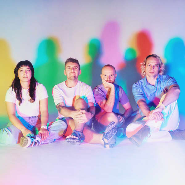 The Beths - a woman with long dark hair and four men - sit in a row with colourful shapes on the wall behind them.