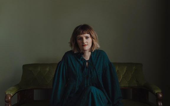 Composer Claire Cowan sits on a green velvet sofa.