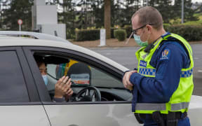 A police officer speaks to a driver wanting to leave the city at a COVID-19 check point setup at the southern boundary in Auckland on August 14, 2020.