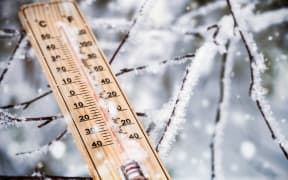 thermometer with plus temperature sticking out of the snow in the winter forest