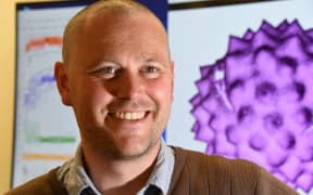 Palynologist Joe Prebble, of GNS Science, standing in front of a false-colour scanning electron microscope image of a pollen of the daisy family.