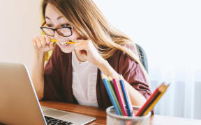 Confused and angry woman bites down on a pencil while looking at a laptop.