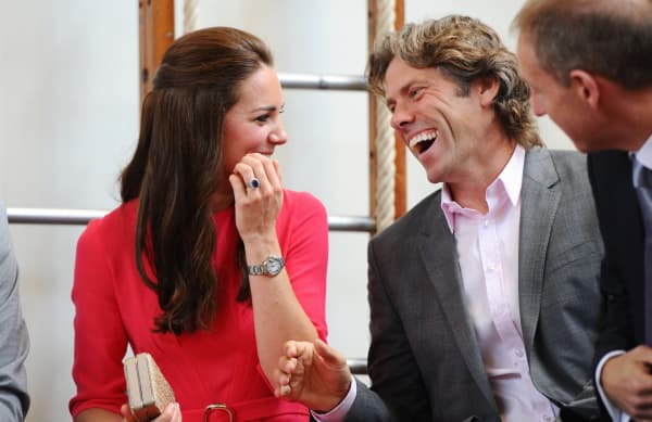John Bishop, wearing a suit, laughs with Catherine, Duchess of Cambridge, who wears a red dress.