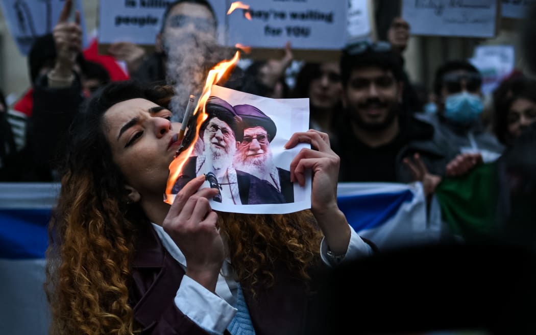 An anti-Iranian regime protester lights a cigarette with a lit paper depicting Ali Khamenei, Supreme Leader of Iran during a gathering outside the US Consulate in Milan, on January 13, 2026. (Photo by Piero CRUCIATTI / AFP)