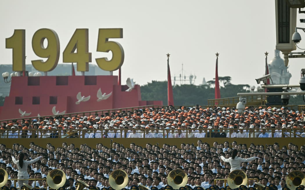 People sing behind a military band before a military parade marking the 80th anniversary of victory over Japan and the end of World War II, in Beijing’s Tiananmen Square on September 3, 2025. (Photo by Pedro Pardo / AFP)