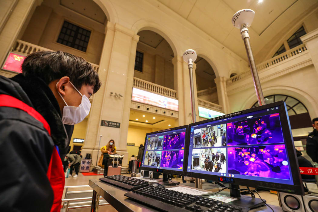 A railway staff member screens arriving passengers with thermal scanners at Hankou station in Wuhan.