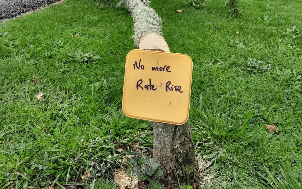Protestor cuts down tree and leaves a 'no more rates rise' sign in its place.