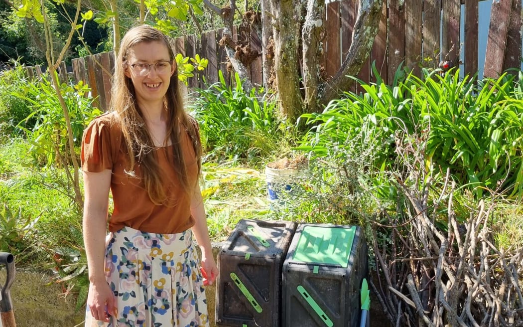 A woman standing in front of two compost roller bins.