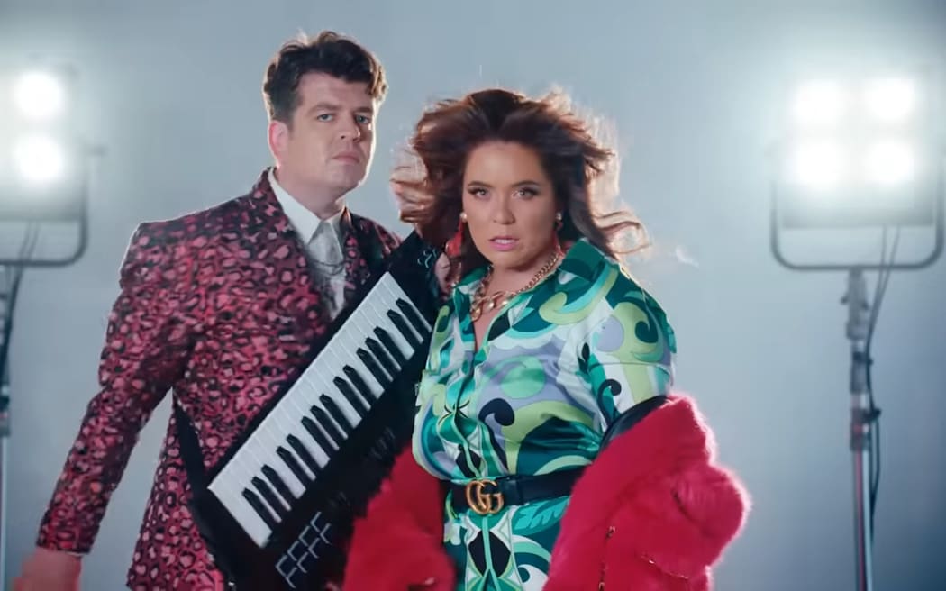 Comedian's Laura Daniel and Joseph Moore standing next to each other. Moore is holding his keyboard. Both are wearing glamourous clothes and makeup.