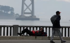 A homeless man lays on the sidewalk near the San Francisco/Oakland Bay Bridge