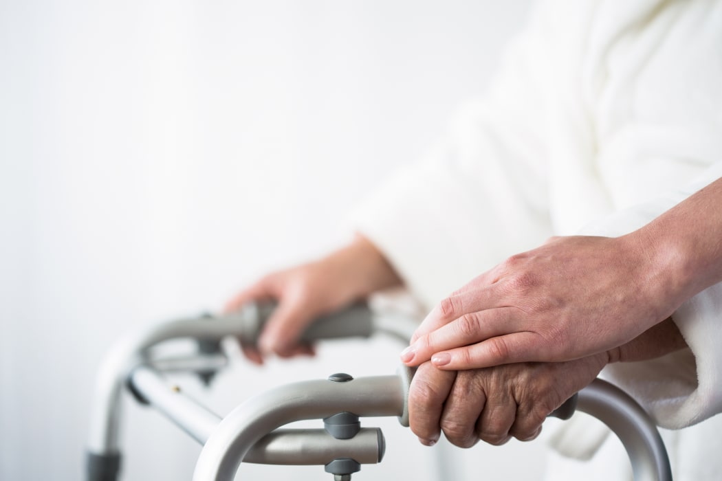 Elderly person using walking aid with help of person.