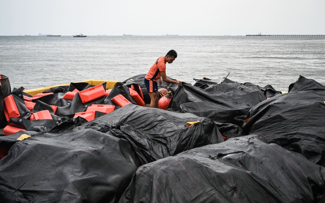 A coast guard personnel arranges an oil spill containment boom to be on standby for deployment at a port in Limay, Bataan on July 25, 2024. A Philippine-flagged tanker carrying 1.4 million litres of industrial fuel oil sank off Manila on July 25, authorities said, as they raced to contain a spill. (Photo by Jam Sta Rosa / AFP)
