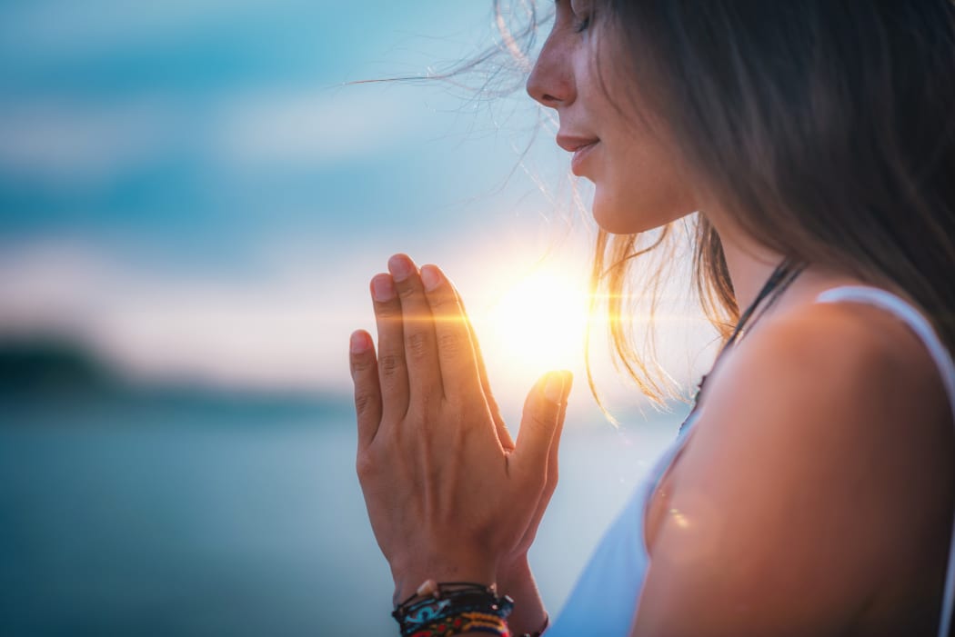 Young woman meditating with her eyes closed, practicing Yoga with hands in prayer position.