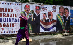A man dressed as the Joker walks past a wall with images of US President Donald Trump and Brazil's right-wing senator and presidential candidate for the Liberal Party (PL) Flavio Bolsonaro during the presidential election on Avenida Paulista in Sao Paulo, Brazil, on October 4, 2026. Brazilians head to the polls in a highly polarized presidential election between incumbent leftist President Luiz Inacio Lula da Silva -seeking a fourth presidential mandate- and right-wing senator Flavio Bolsonaro, who emerged as the leading figure of the conservative movement following the conviction and imprisonment of his father, former president Jair Bolsonaro. (Photo by Pablo PORCIUNCULA / AFP)