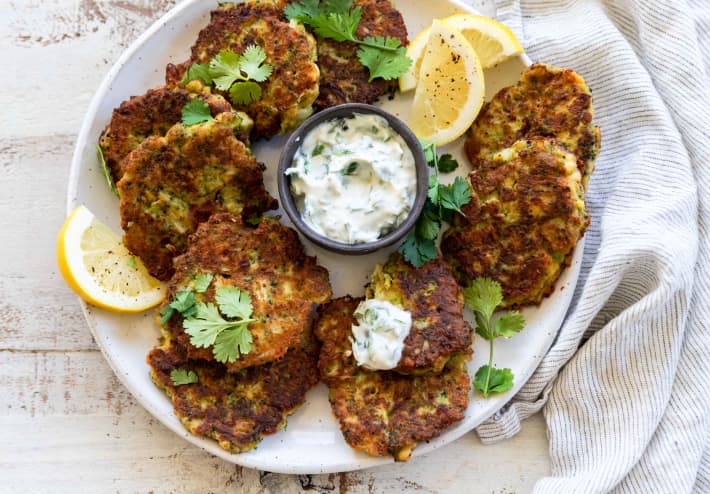 A round plate filled with Broccoli and cottage cheese fritters, sliced lemon and coriander leaves.