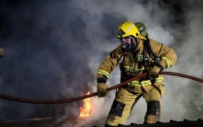 A FENZ firefighter works in breathing gear, amid smoke.