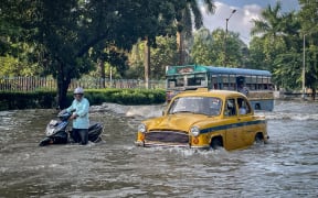 A scooter, bus, and yellow taxi move through a flooded road after heavy rainfall in Kolkata, West Bengal, India, on September 23, 2025. (Photo by Yousuf Sarfaraz/NurPhoto) (Photo by Yousuf Sarfaraz / NurPhoto via AFP)