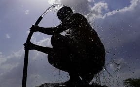 A man is silhouetted against the sun as he bathes on a hot summer day at a village on the outskirts of Ajmer on June 11, 2024 amid heatwave. India's heatwave is the longest ever to hit the country, the government's top weather expert said on June 10 as he warned people will face increasingly oppressive temperatures. Parts of northern India have been gripped by a heatwave since mid-May, with temperatures soaring over 45 degrees Celsius (113 degrees Fahrenheit). (Photo by Himanshu SHARMA / AFP)