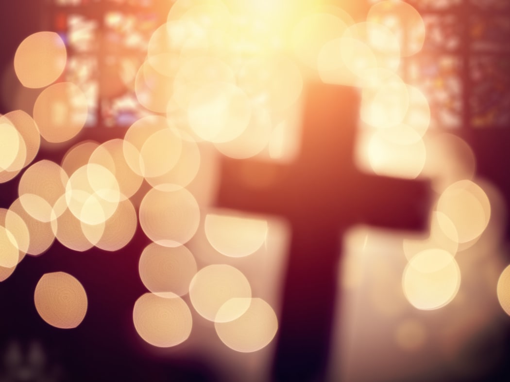 Abstract defocussed cross silhouette in church interior against stained glass window.