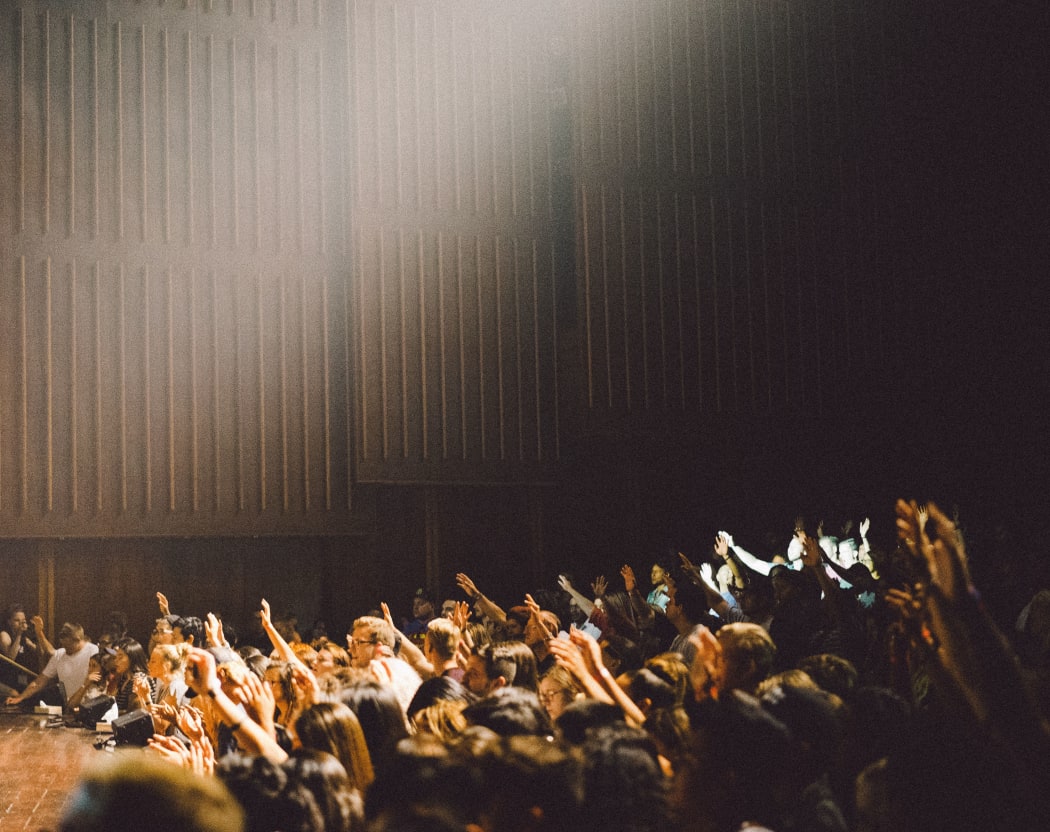 An audience in an auditorium, voting with raised hands.