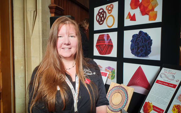 Jeannette McLeod, Maths Craft director stands in front of a poster with pictures of crafts on it.