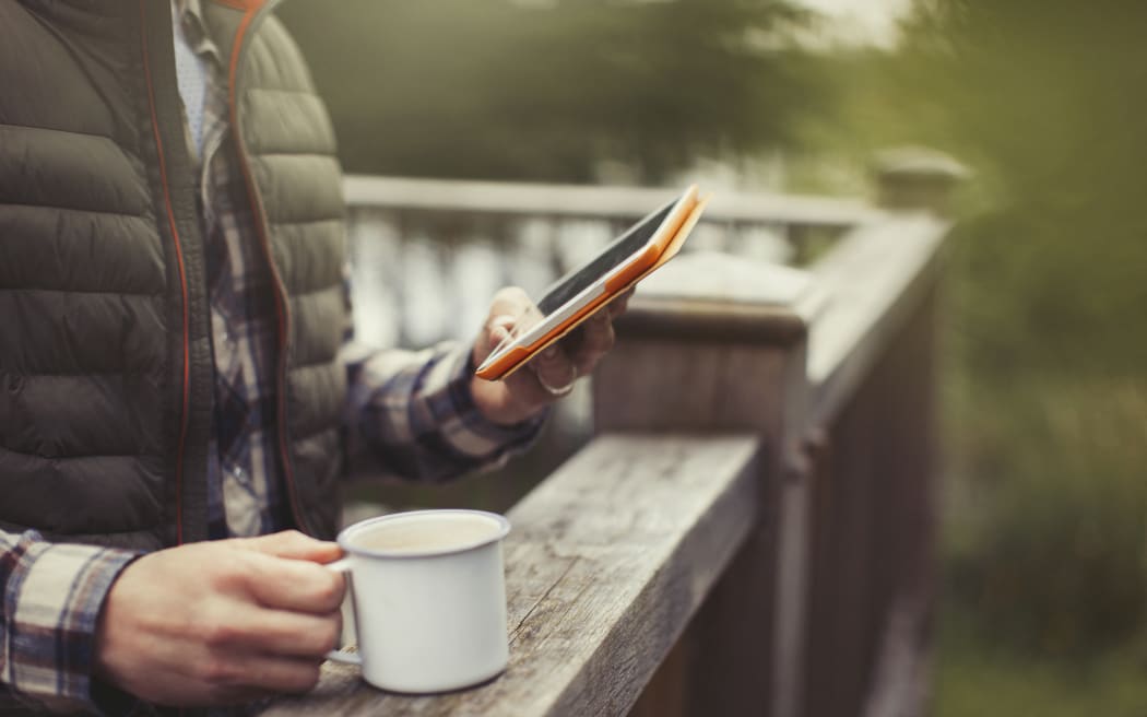 Man drinking coffee using digital tablet on balcony. (Photo by CAIA IMAGE/SCIENCE PHOTO LIBRARY / NEW / Science Photo Library via AFP)